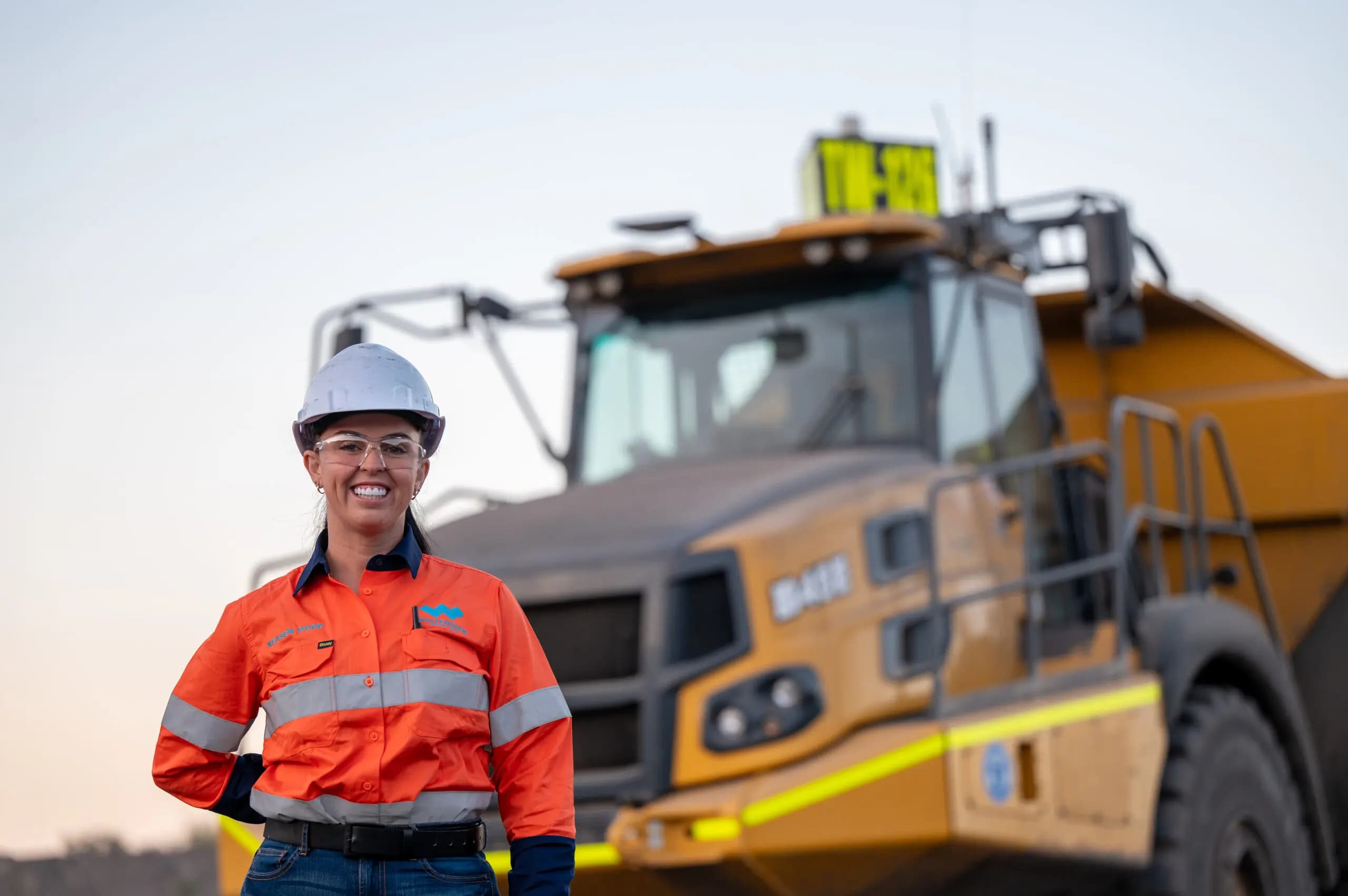 Smiling mine operator in high-vis standing in front of a haul truck