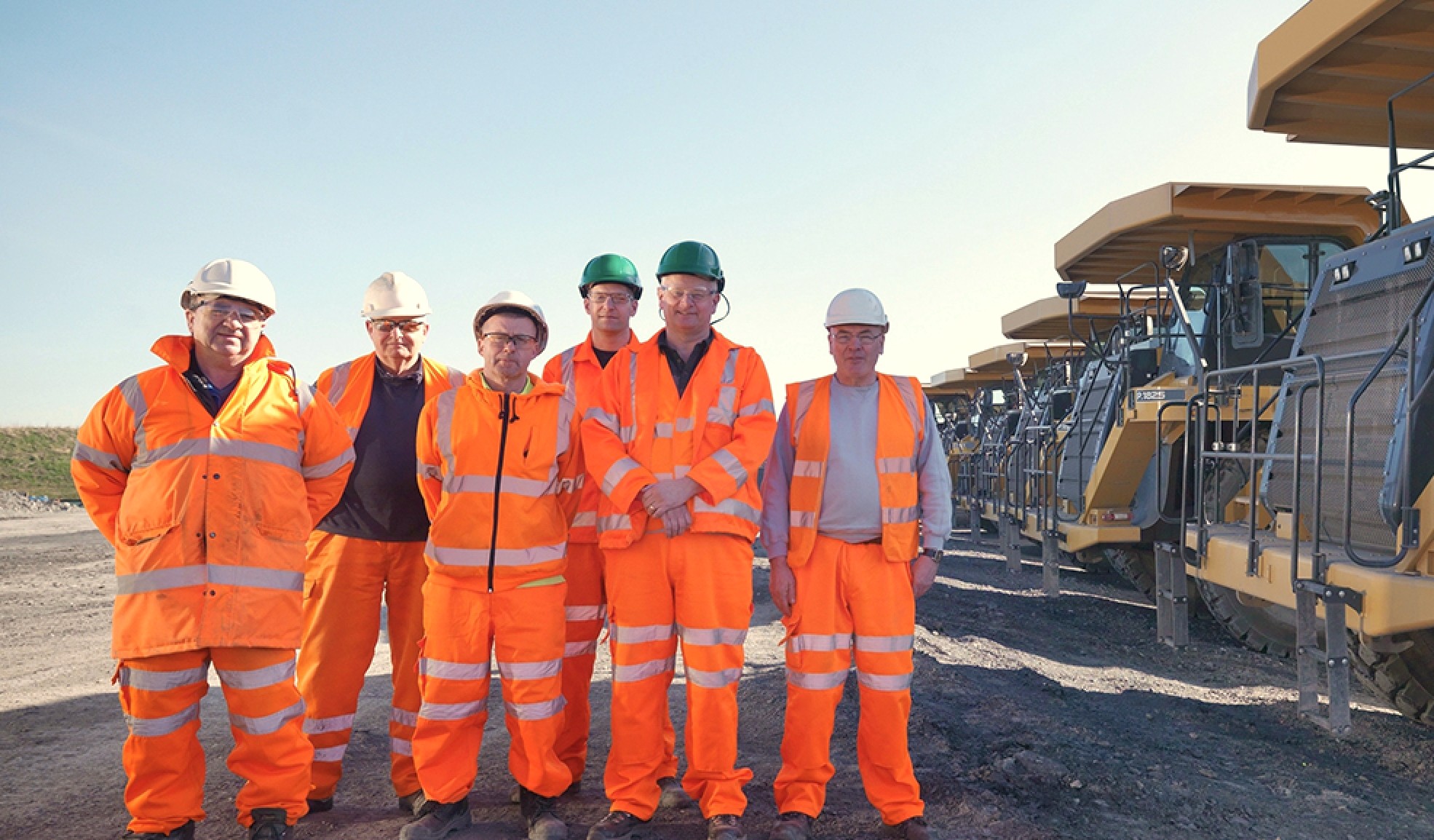 A FIFO mining crew standing in front of a line of haul trucks